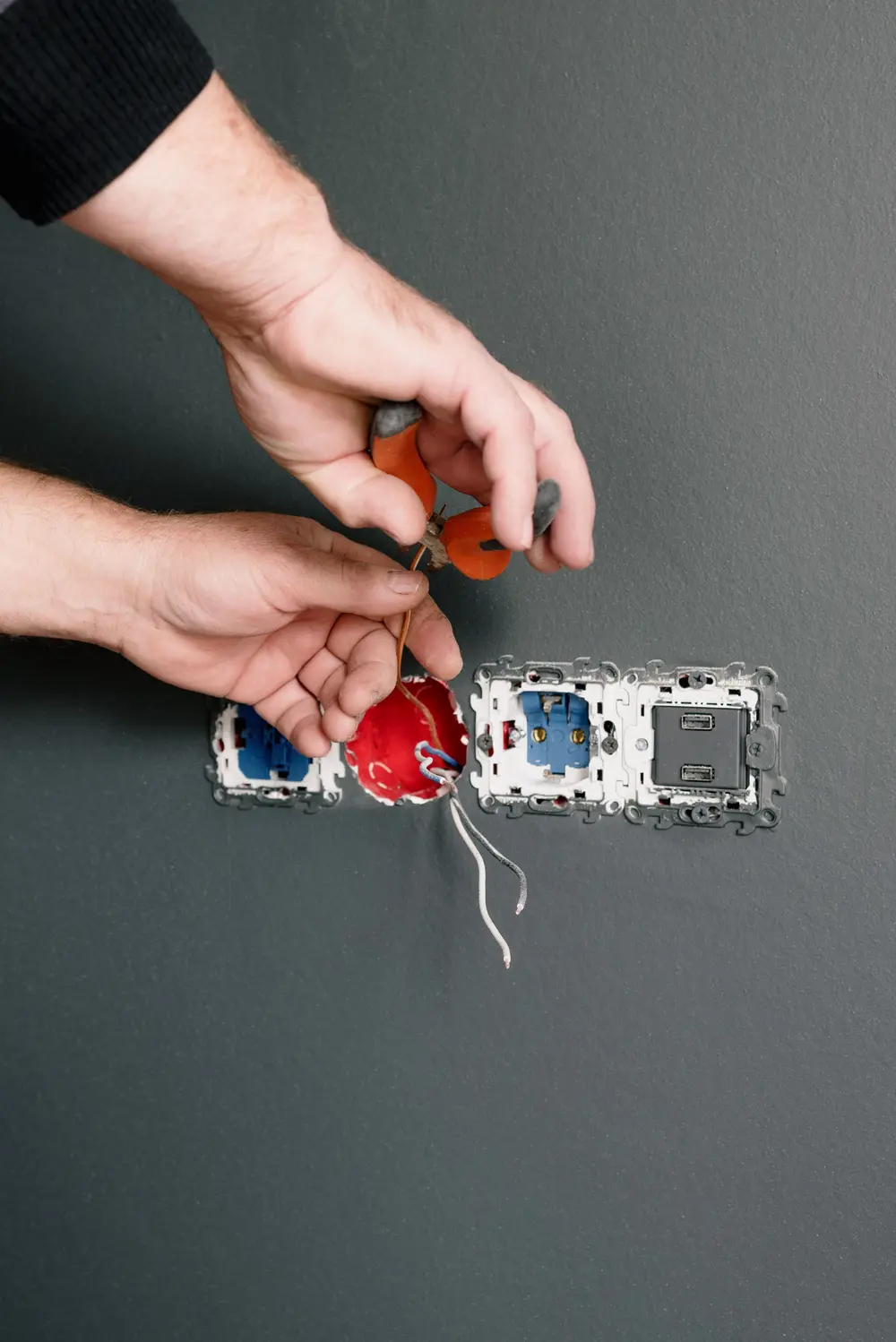 Illustrative stock photo of hands preparing wiring beside uncovered wall sockets